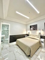 Un dormitorio moderno con una cama grande, cabina de ducha de vidrio y piso de mármol.