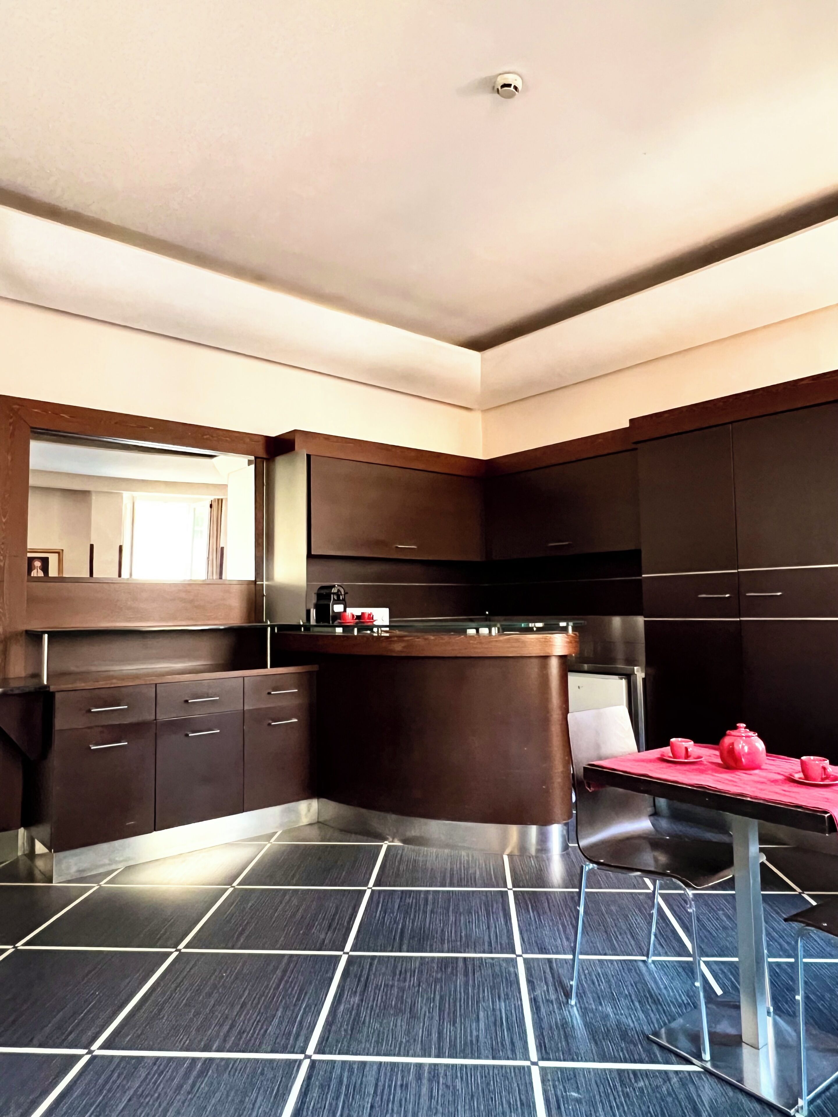 A modern kitchen with dark cabinetry, a central island, and a red table with teapots.