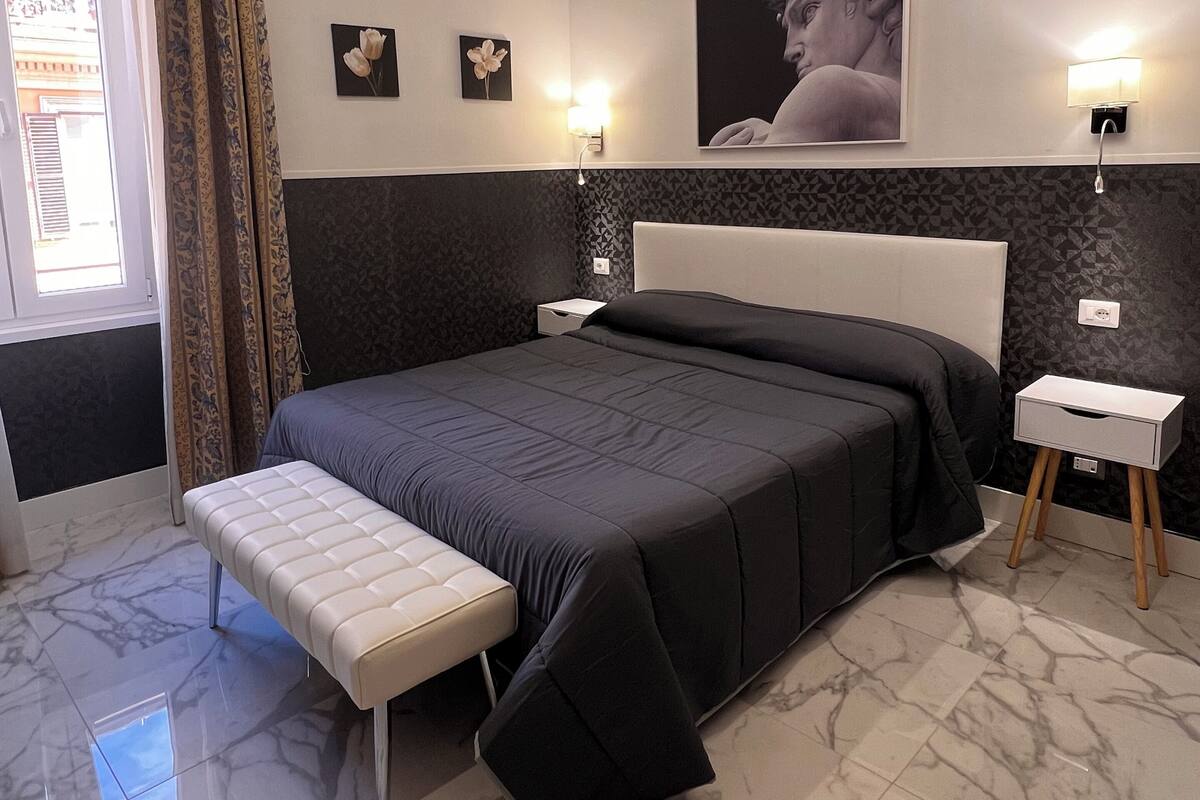 A modern bedroom with a large bed, a bedside table, a bench, and a nightstand.