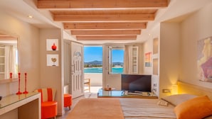 Habitación de hotel moderna con una cama grande, un escritorio y un televisor. La habitación tiene vista a la playa y al mar.