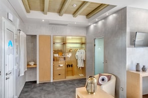 A modern bathroom with a shower, a vanity with a mirror, and a wooden cabinet with towels and toiletries. - Nissaki Beach Hotel (Naxos)