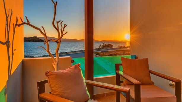 Un balcón con vista al atardecer sobre el mar, dos sillas de madera y una rama decorativa.
