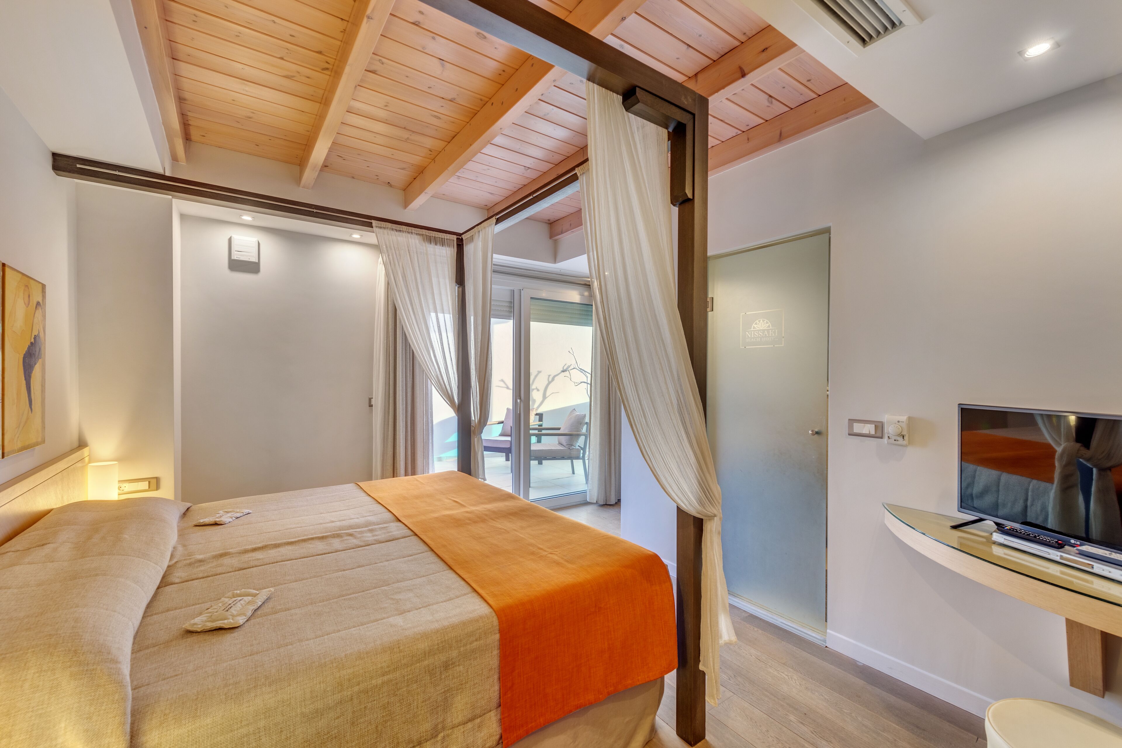 A bedroom with a bed, curtains, a TV, and a glass table.