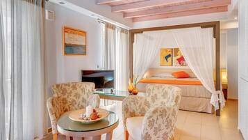 Una habitación de hotel con una cama, televisión, una mesita de vidrio con sillas y un cuadro en la pared.