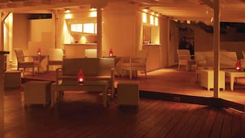 Eine Terrasse im Freien mit Holzboden, weißen Korbmöbeln und stimmungsvoller Beleuchtung.