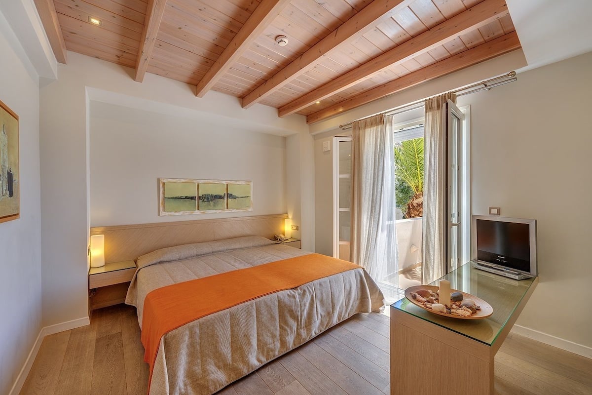 A bedroom with a bed, a television on a glass table, and a window with curtains.