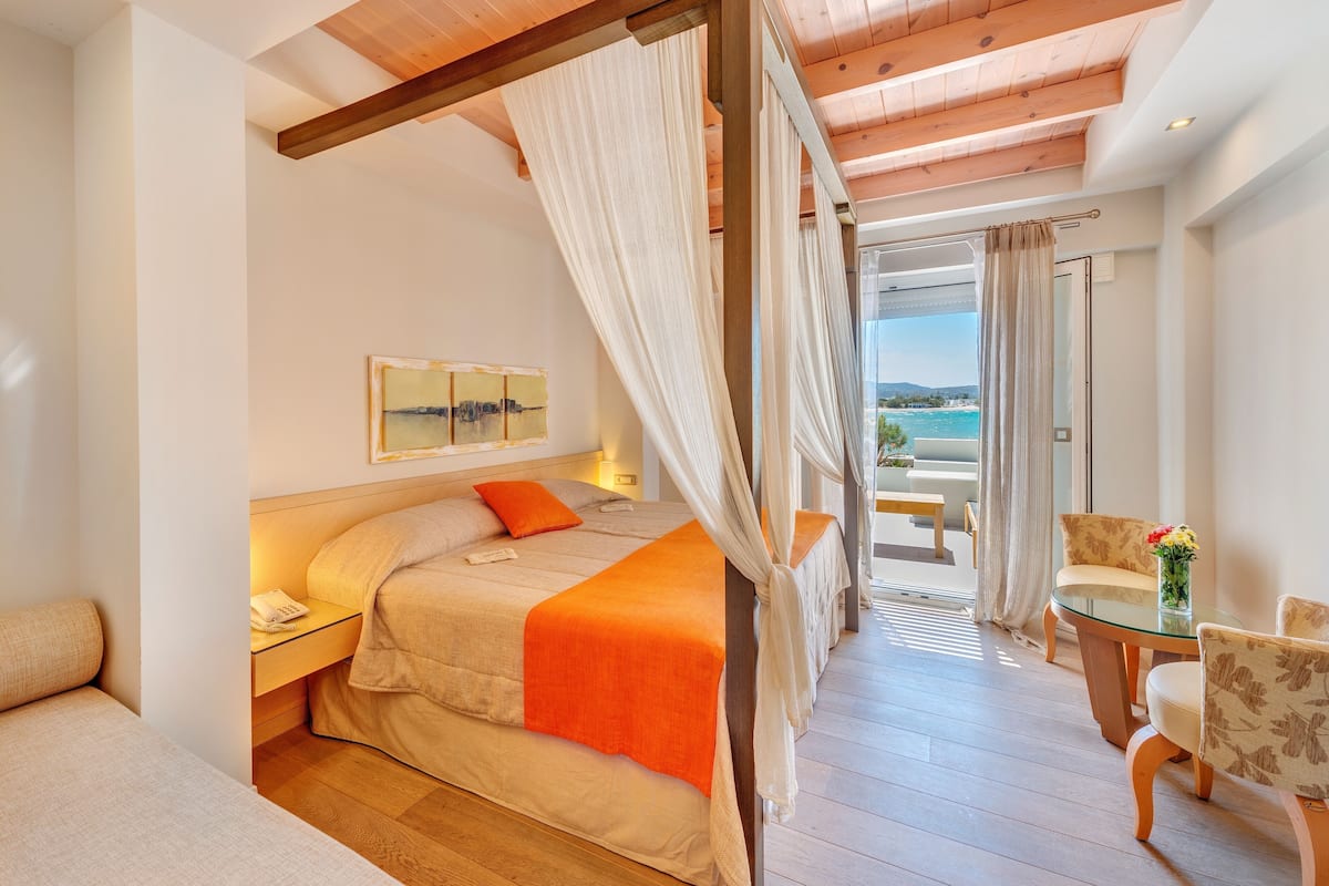 A bedroom with a bed, bedside table, and a view of the sea.
