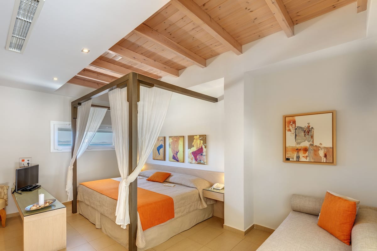 A bedroom with a canopy bed, a sofa, a bedside table, and artwork on the walls.