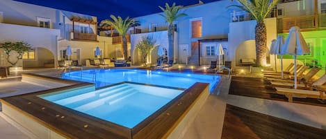 A swimming pool with lounge chairs and umbrellas, surrounded by palm trees and a wooden deck.
