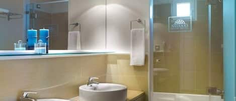 Un baño moderno con dos lavamanos, cabina de ducha de vidrio y un cartel visible del Hotel Nissaki Beach.