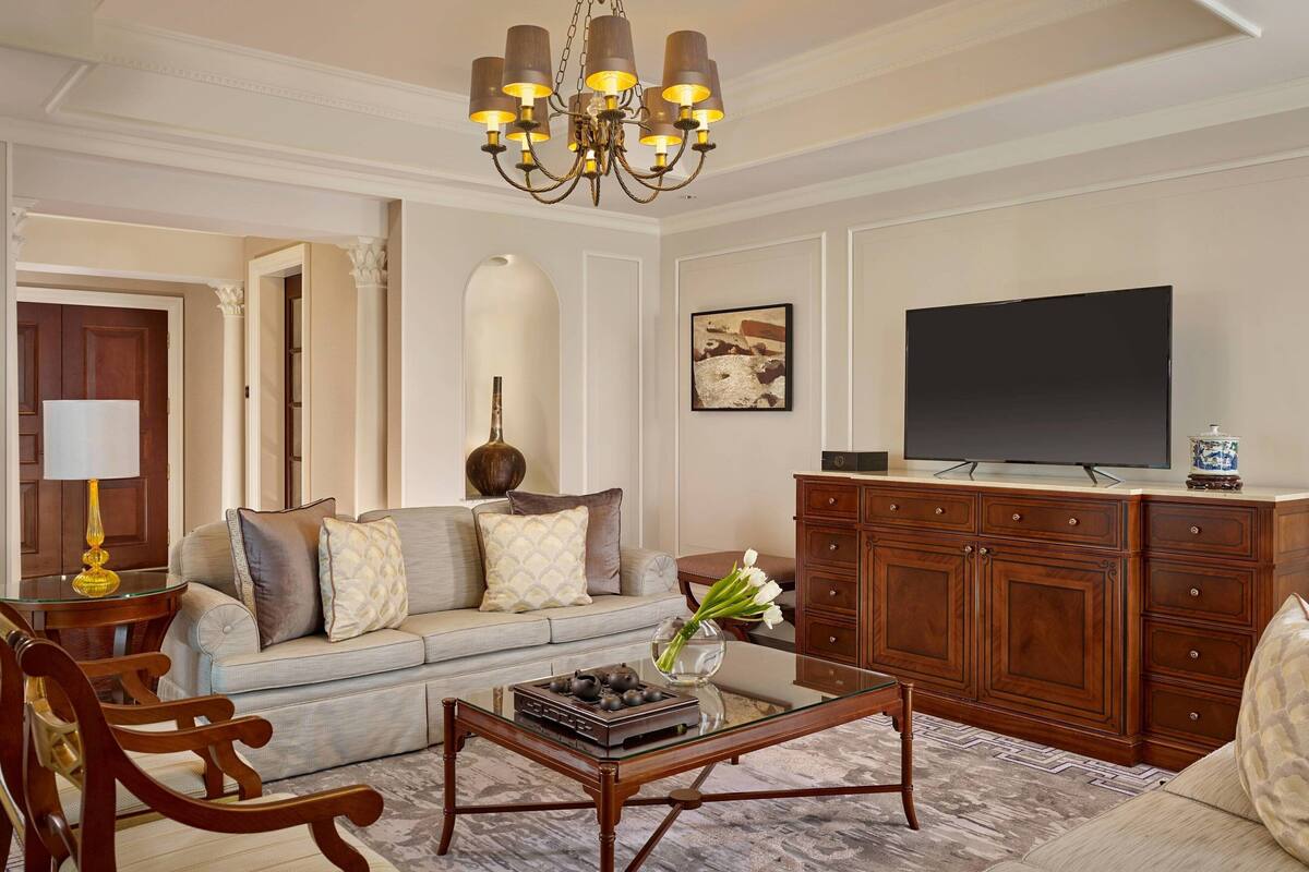 A living room with a sofa, coffee table, TV, wooden cabinet, and a chandelier.