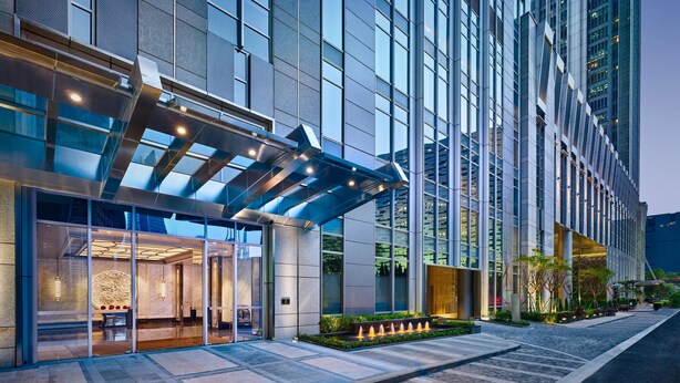 A modern hotel entrance with a glass facade, a covered entrance area, and a landscaped garden with a water feature. - The Ritz-Carlton, Guangzhou (Guangzhou)
