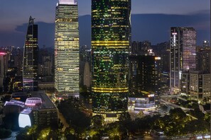 A cityscape at night with illuminated skyscrapers, a curved building with a green-lit facade, and a modern architectural structure with a unique roof design.