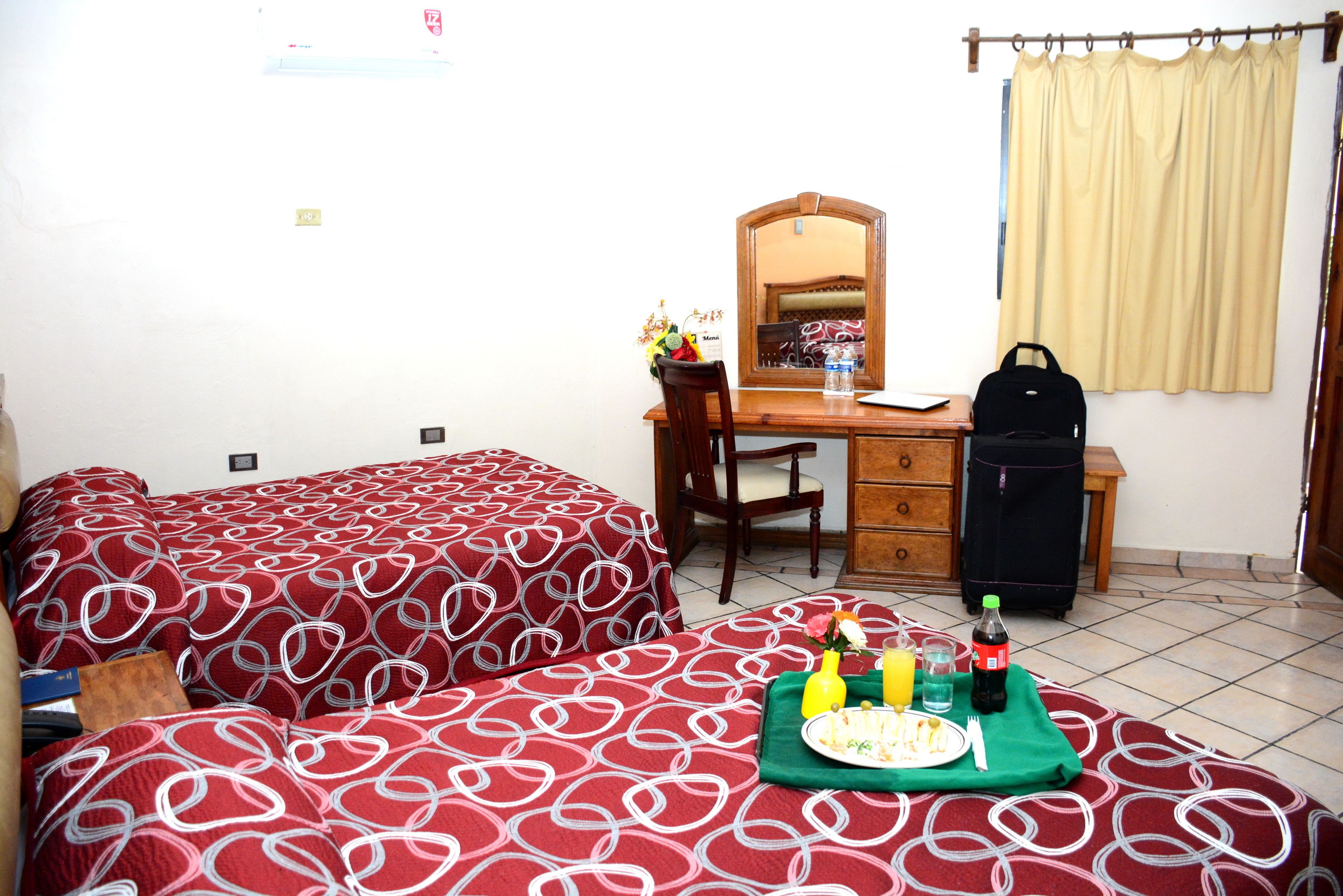 A hotel room with two beds, a desk, a chair, a dresser, and a suitcase.