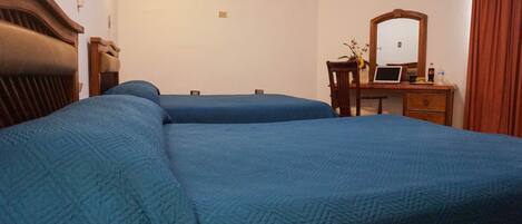 A hotel room with two beds, a desk with a laptop, a mirror, and an air conditioning unit on the wall.