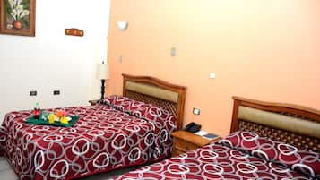 A hotel room with two beds, a bedside table with a lamp, and a small table with a tray of breakfast items.