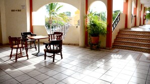 A lobby with a tiled floor, wooden chairs, a table, potted plants, and a staircase with red accents. - Hotel Las Fuentes (Los Mochis)