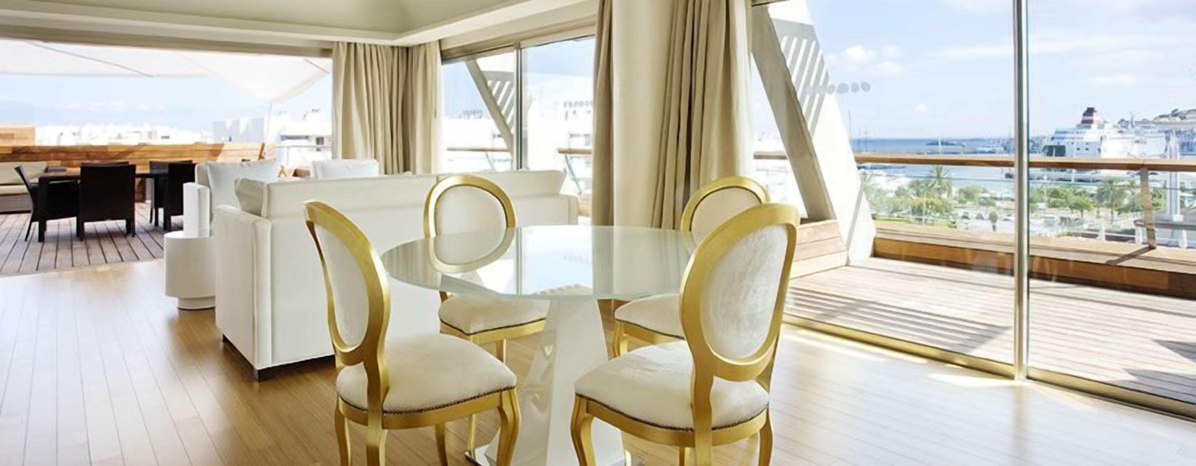 Een moderne eethoek met een glazen tafel en gouden stoelen, met uitzicht op een stadsbeeld.