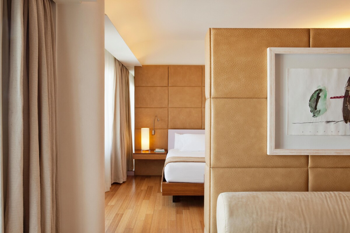 Una habitación de hotel con cama, mesita de noche, lámpara y un cuadro en la pared.