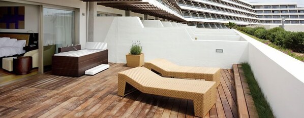 Un espacio lounge moderno al aire libre con terraza de madera, un sofá y dos sillones.
