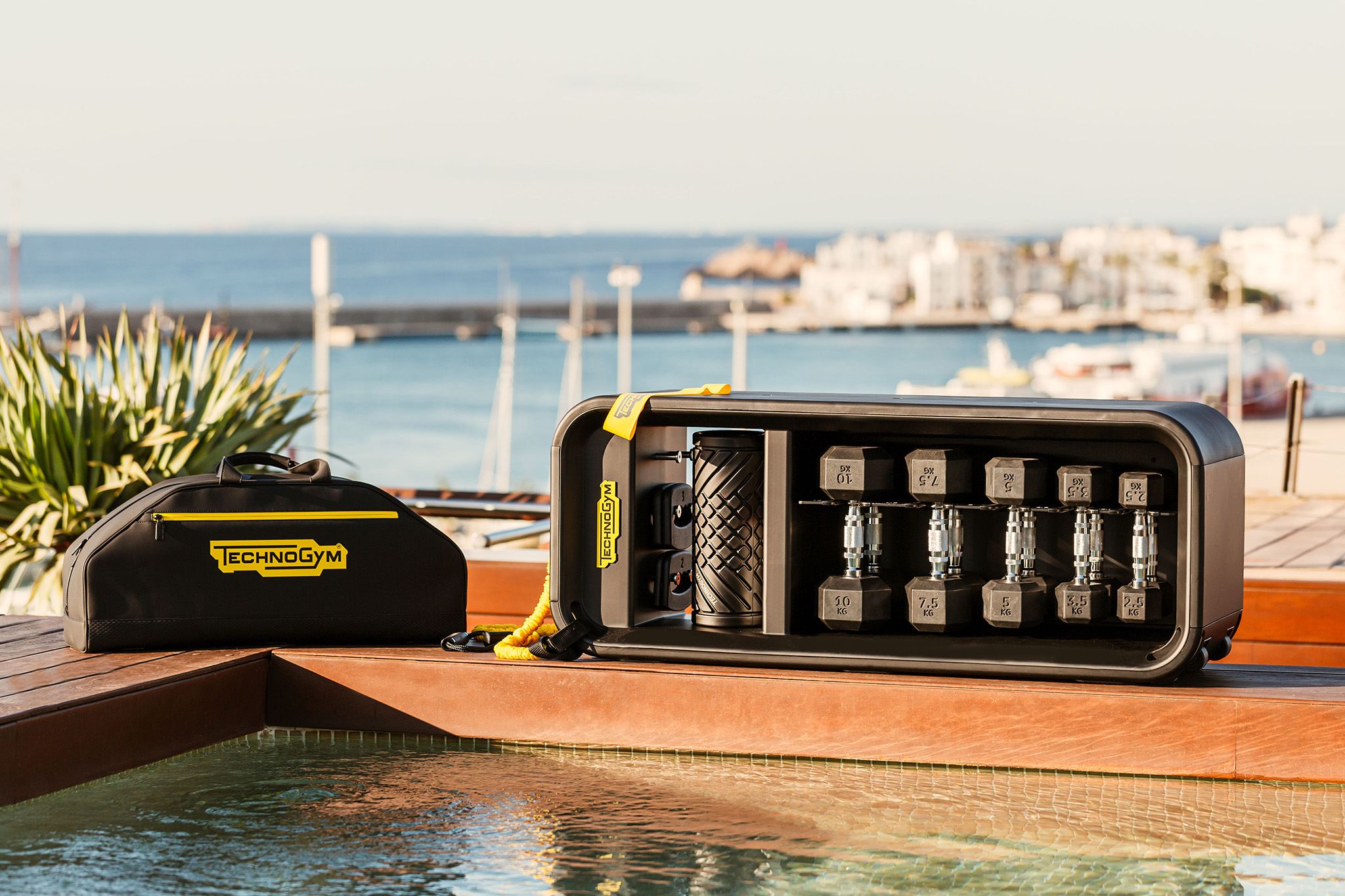 Area piscina con attrezzature fitness Technogym e una borsa da palestra.