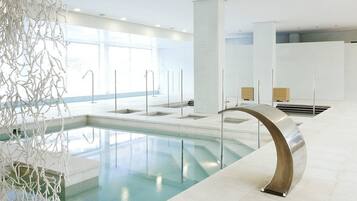 Ein moderner, überdachter Poolbereich mit großen Glaswänden, einem zentralen Schwimmbecken und minimalistischem Design.