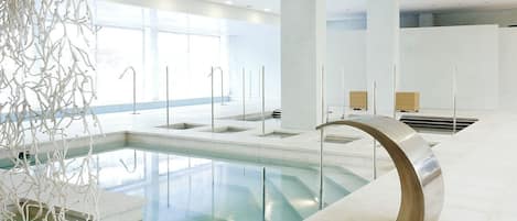 A modern indoor pool area with clear glass walls, a central pool, and minimalist design elements.