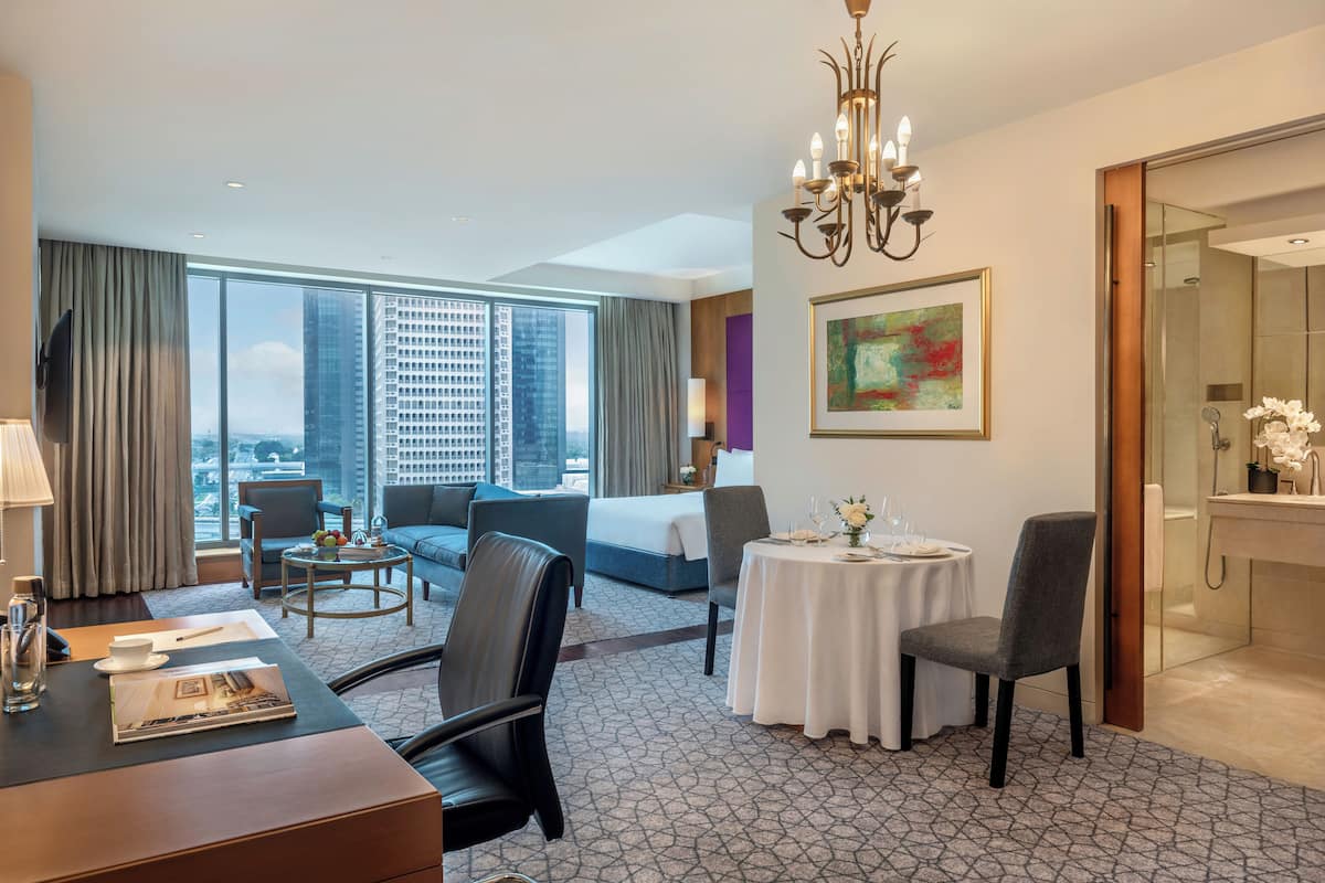 A hotel room with a large window, a bed, a dining table, and a bathroom.