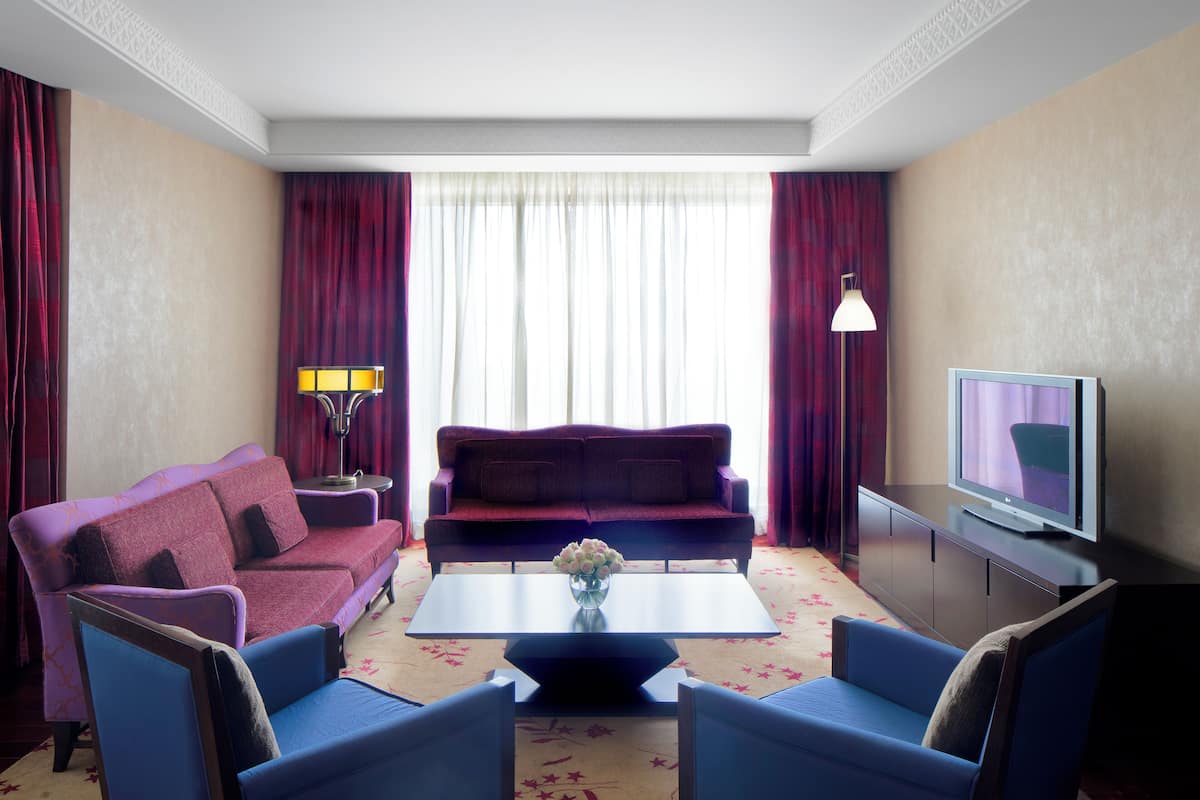 A hotel room with a purple sofa, a blue armchair, a coffee table, a TV, and a lamp.