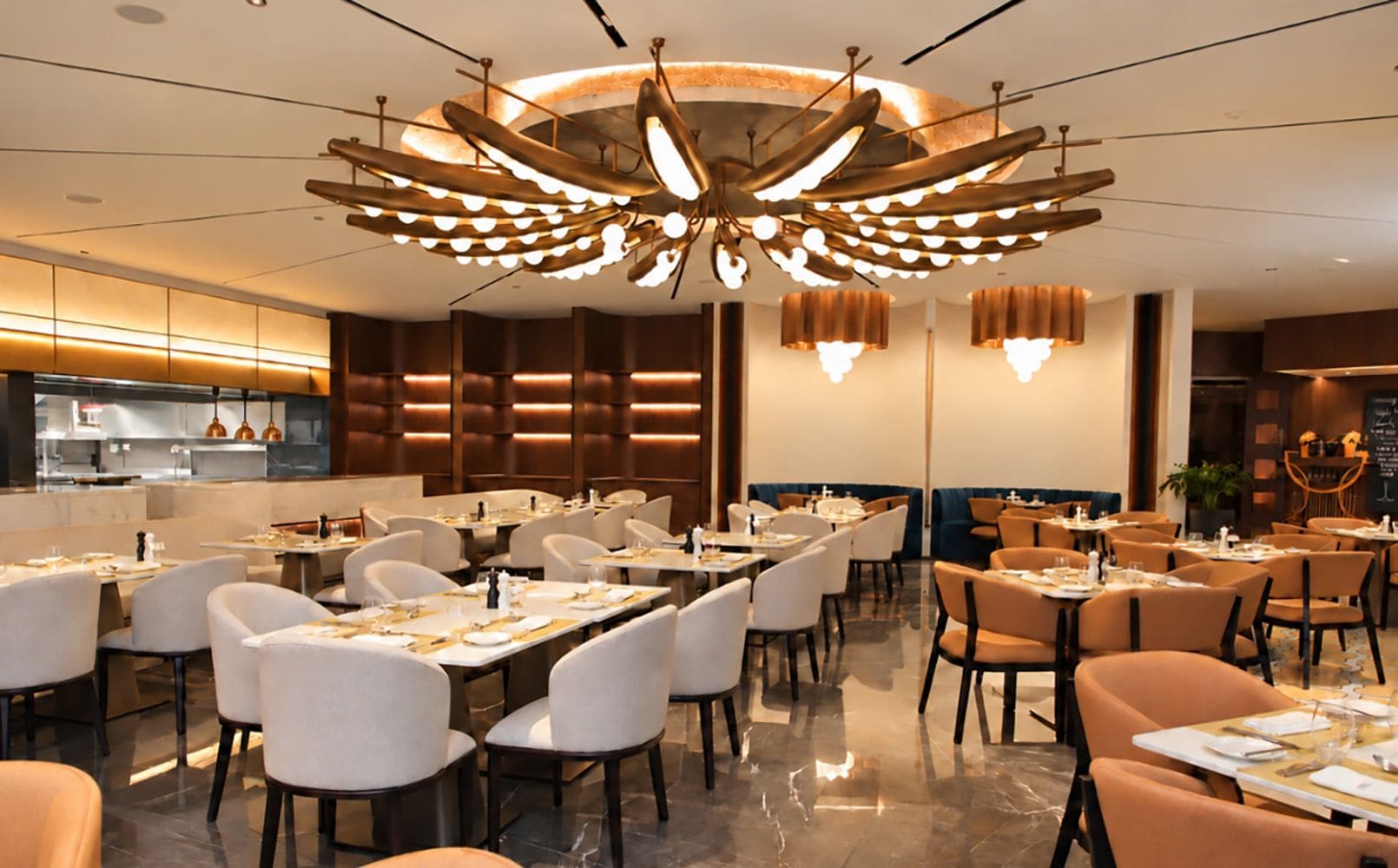 A modern dining area with multiple tables and chairs, a distinctive ceiling light fixture, and a visible kitchen area in the background.