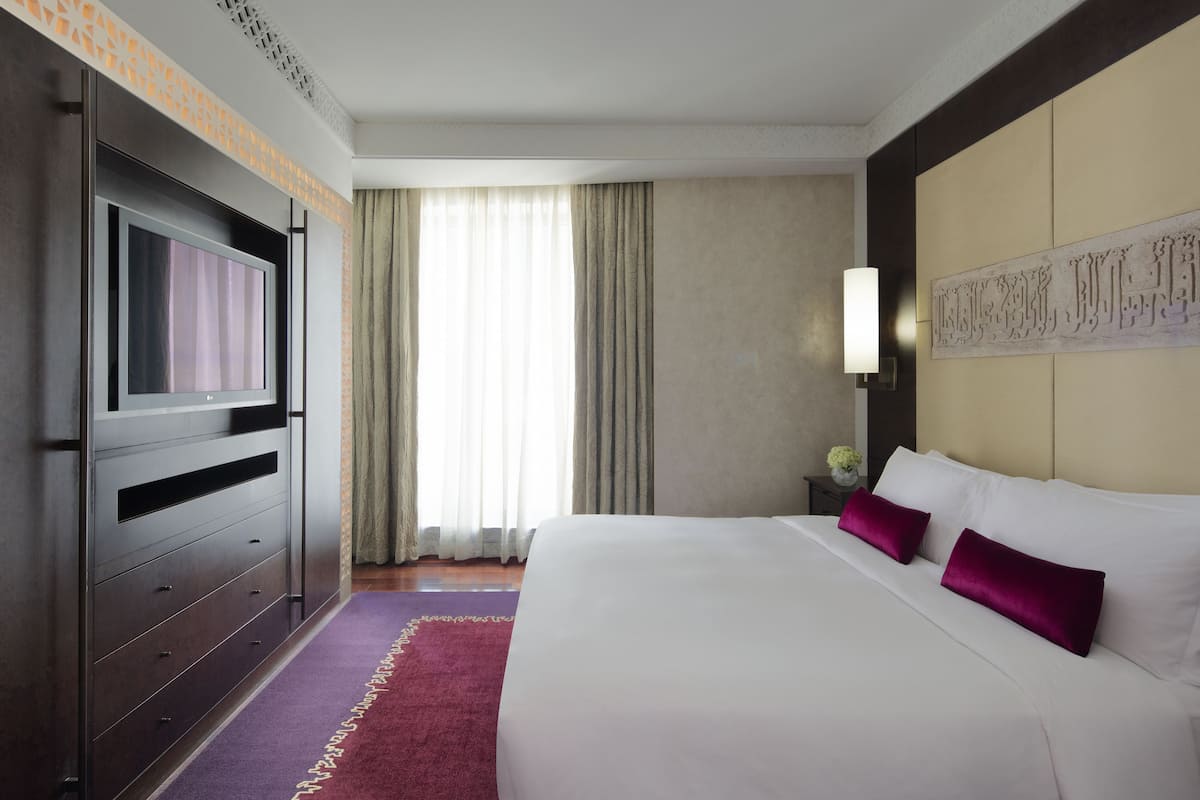 A hotel room with a large bed, a TV, a nightstand, a lamp, and a decorative wall piece.