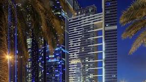 A nighttime view of a modern cityscape with tall buildings, palm trees, and a well-lit street. - The H Dubai (Dubai)