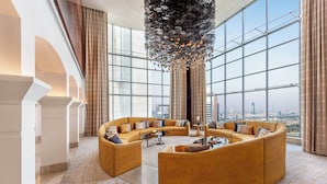 A spacious, modern lounge with a large, curved sofa arrangement and a city view through expansive windows. - The H Dubai (Dubai)