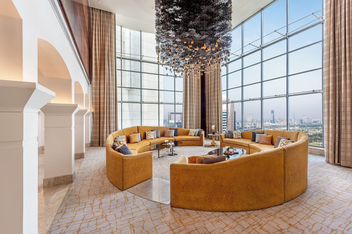 A spacious, modern lounge with a large, curved sofa arrangement and a city view through expansive windows.