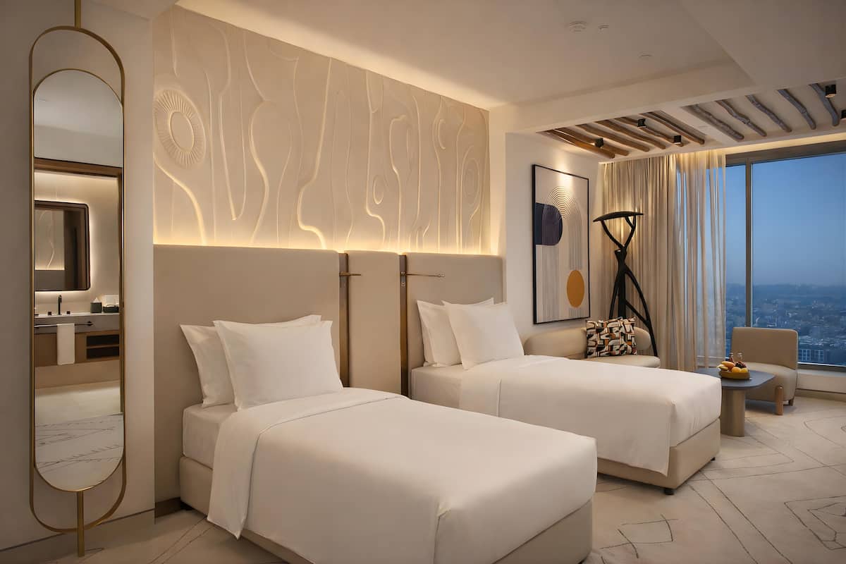 A modern hotel room with two beds, a large mirror, a city view, and a contemporary design.