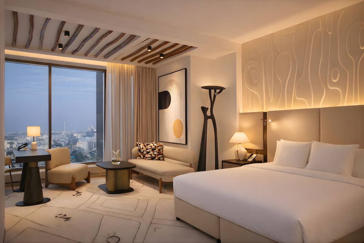 A hotel room with a large bed, a sofa, a desk, and a view of the city.