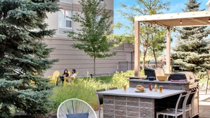 An outdoor patio with a barbecue grill, seating area, and a view of a building in the background. - Homewood Suites by Hilton Toronto-Markham (Markham)