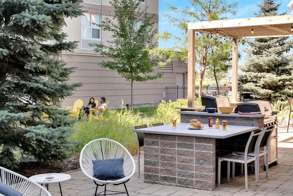 An outdoor patio with a barbecue grill, seating area, and a view of a building in the background. - Homewood Suites by Hilton Toronto-Markham (Markham)