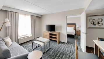 Habitación de hotel con sofá, una mesita, televisor sobre un mueble de madera, cama y escritorio.