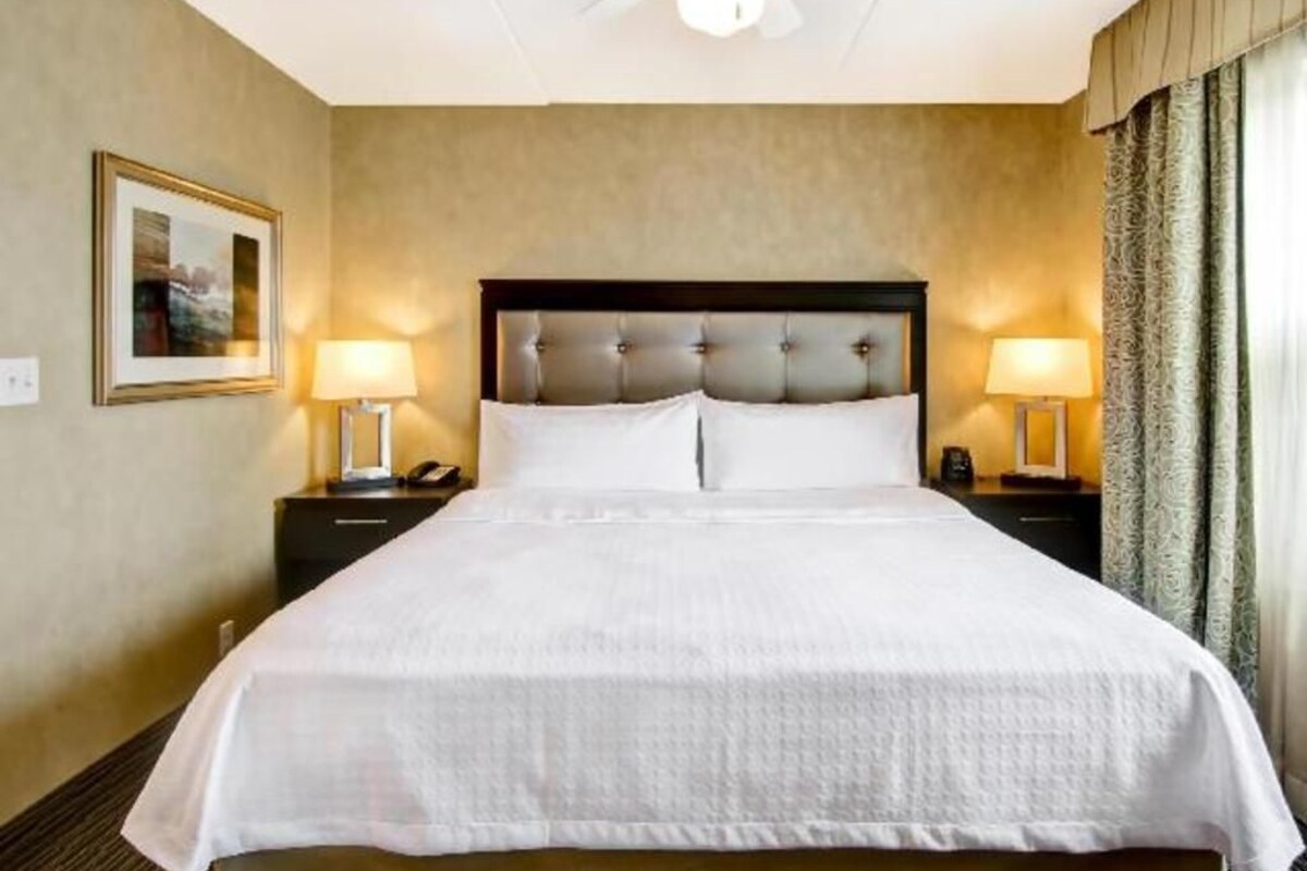 A hotel room with a large bed, two bedside lamps, a ceiling fan, and a framed picture on the wall.
