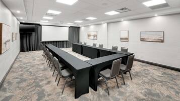 A conference room with a long table, chairs, a projector screen, and artwork on the walls.