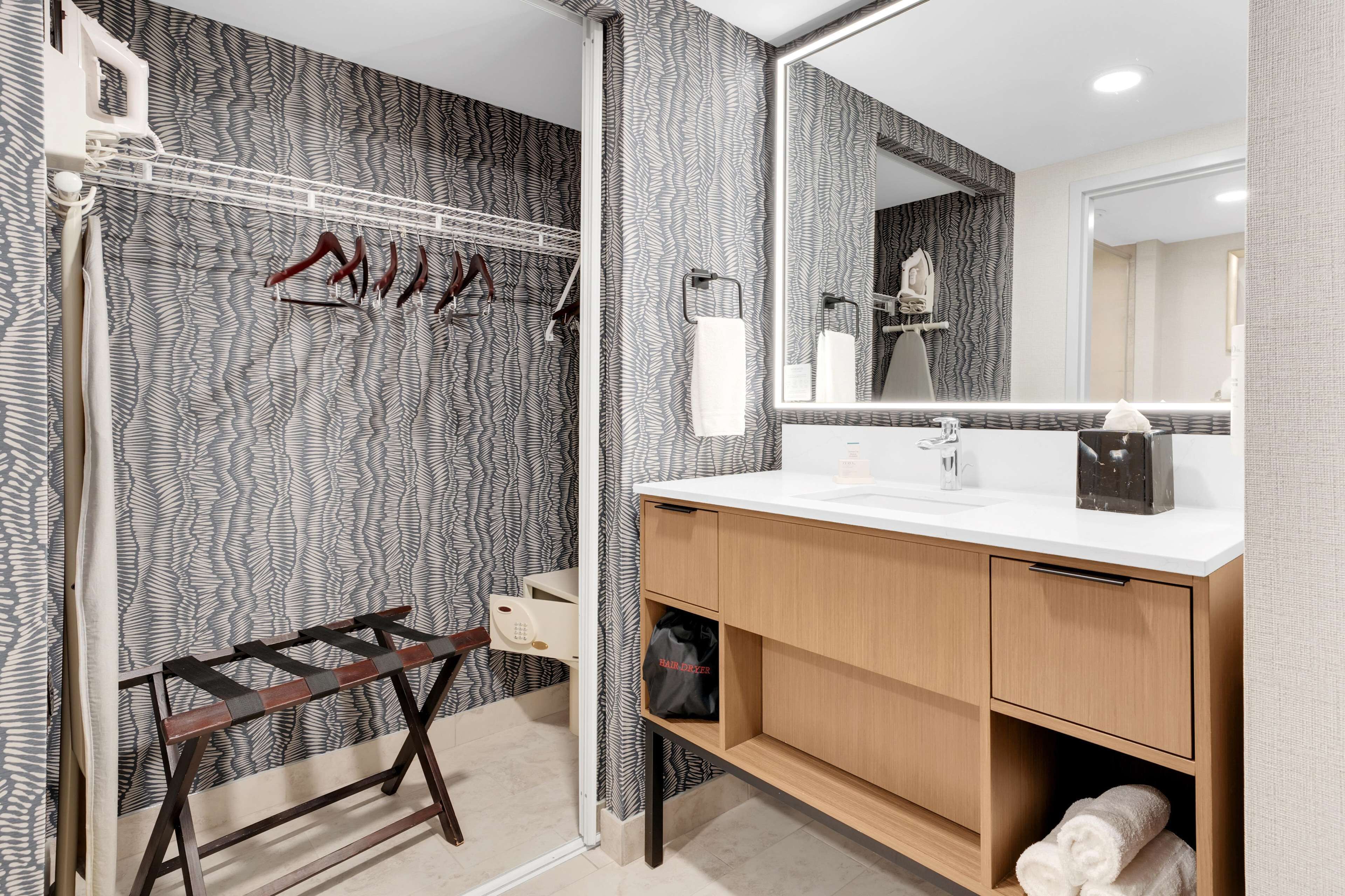 A modern bathroom with a patterned wallpaper, a wooden vanity, a mirror, and a towel rack.