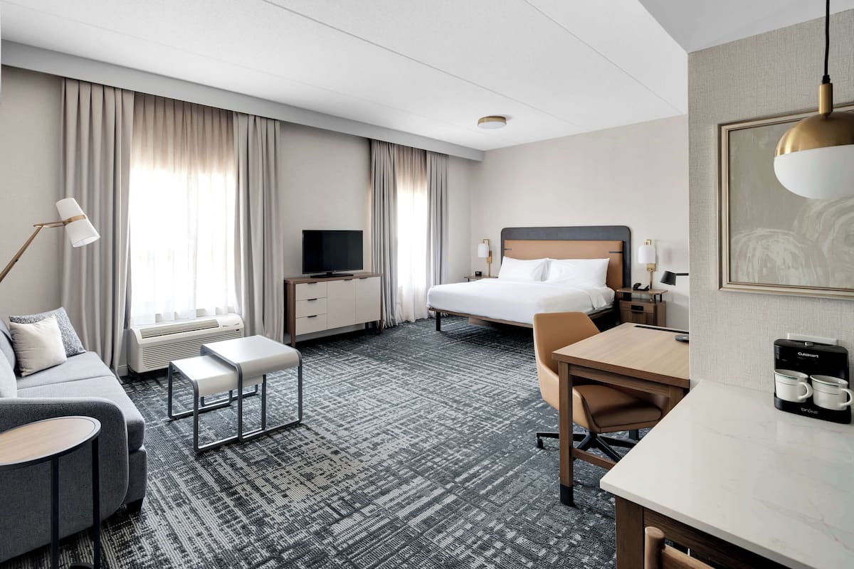A hotel room with a bed, a sofa, a desk, a TV, and a coffee maker.