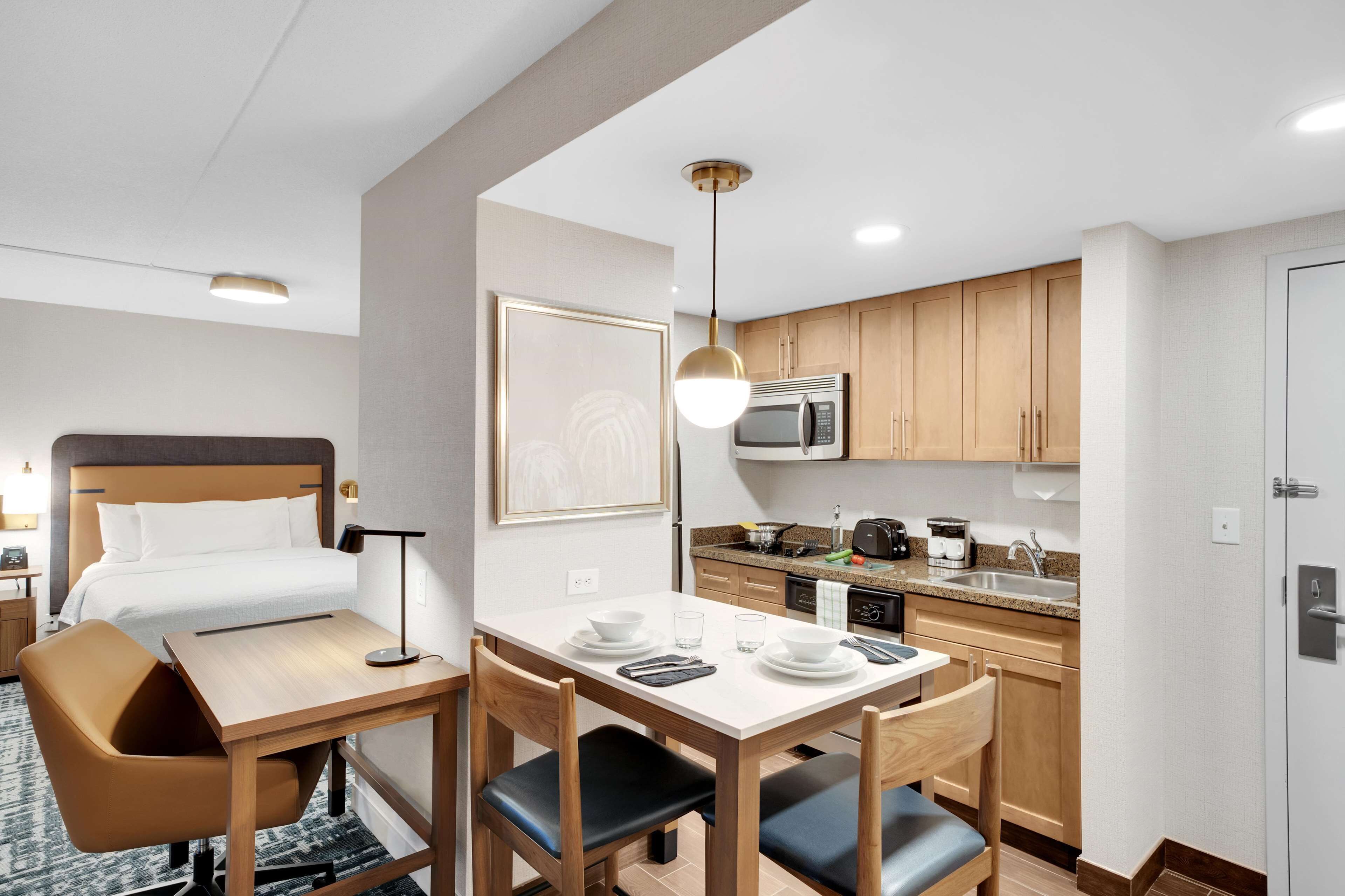 A compact hotel room with a bed, a small dining table with chairs, a kitchenette, and a bathroom.