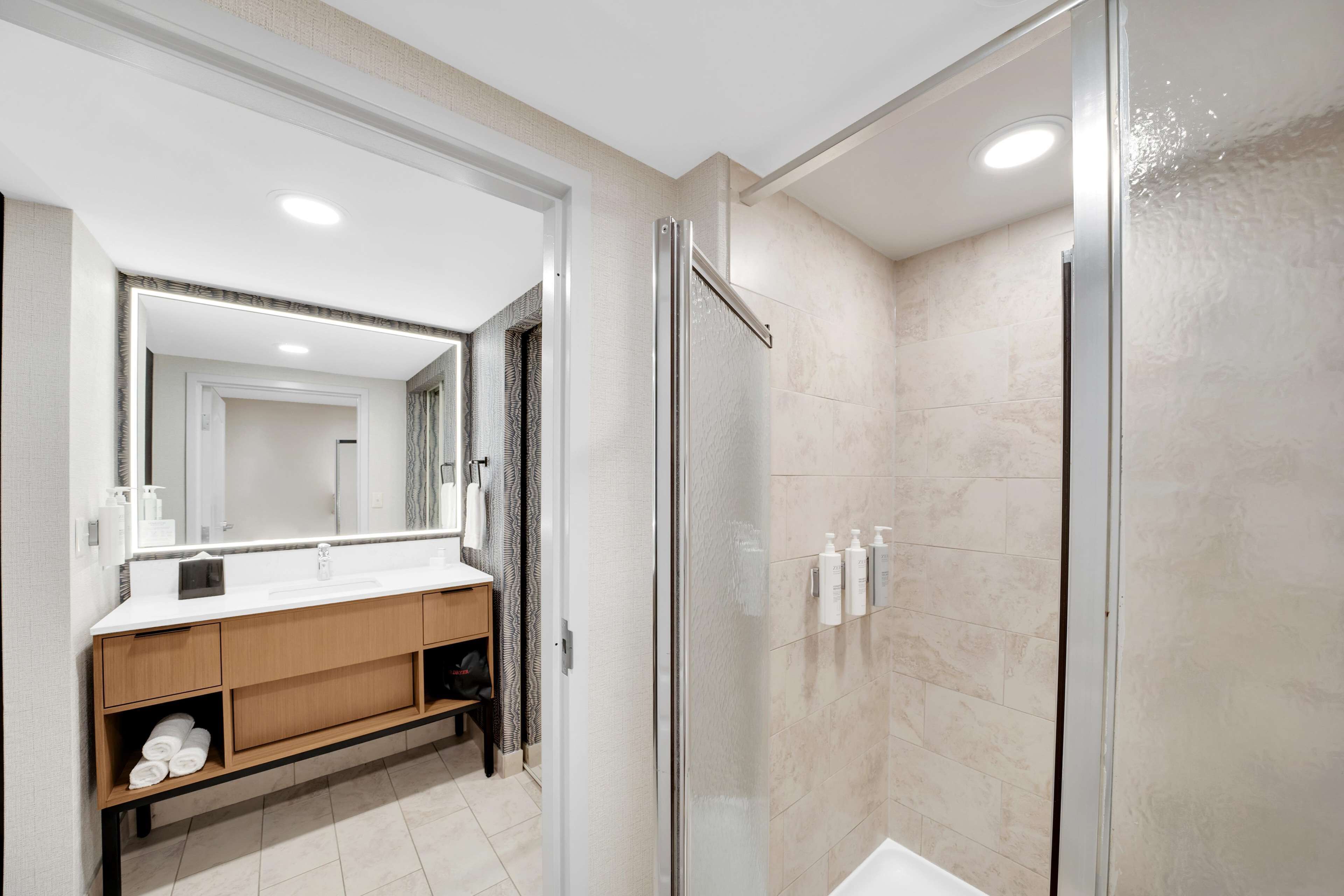 A modern bathroom with a glass-enclosed shower, a white vanity with a mirror, and a beige tiled floor.