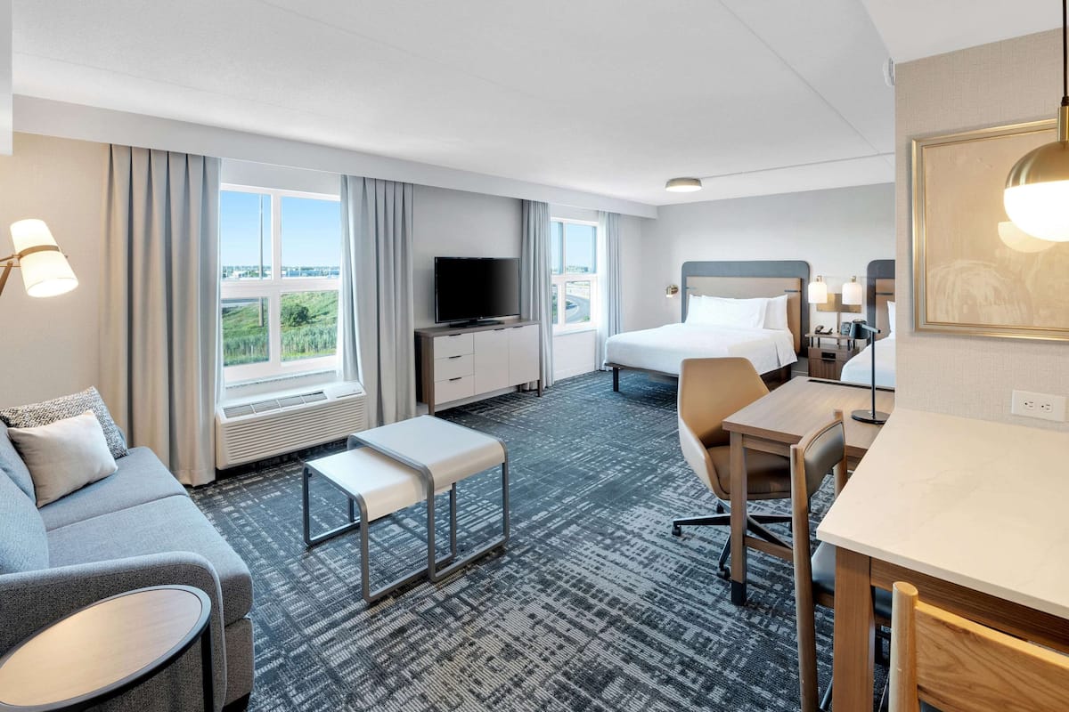 A hotel room with a bed, a desk, a chair, a sofa, a TV, and a window with curtains.