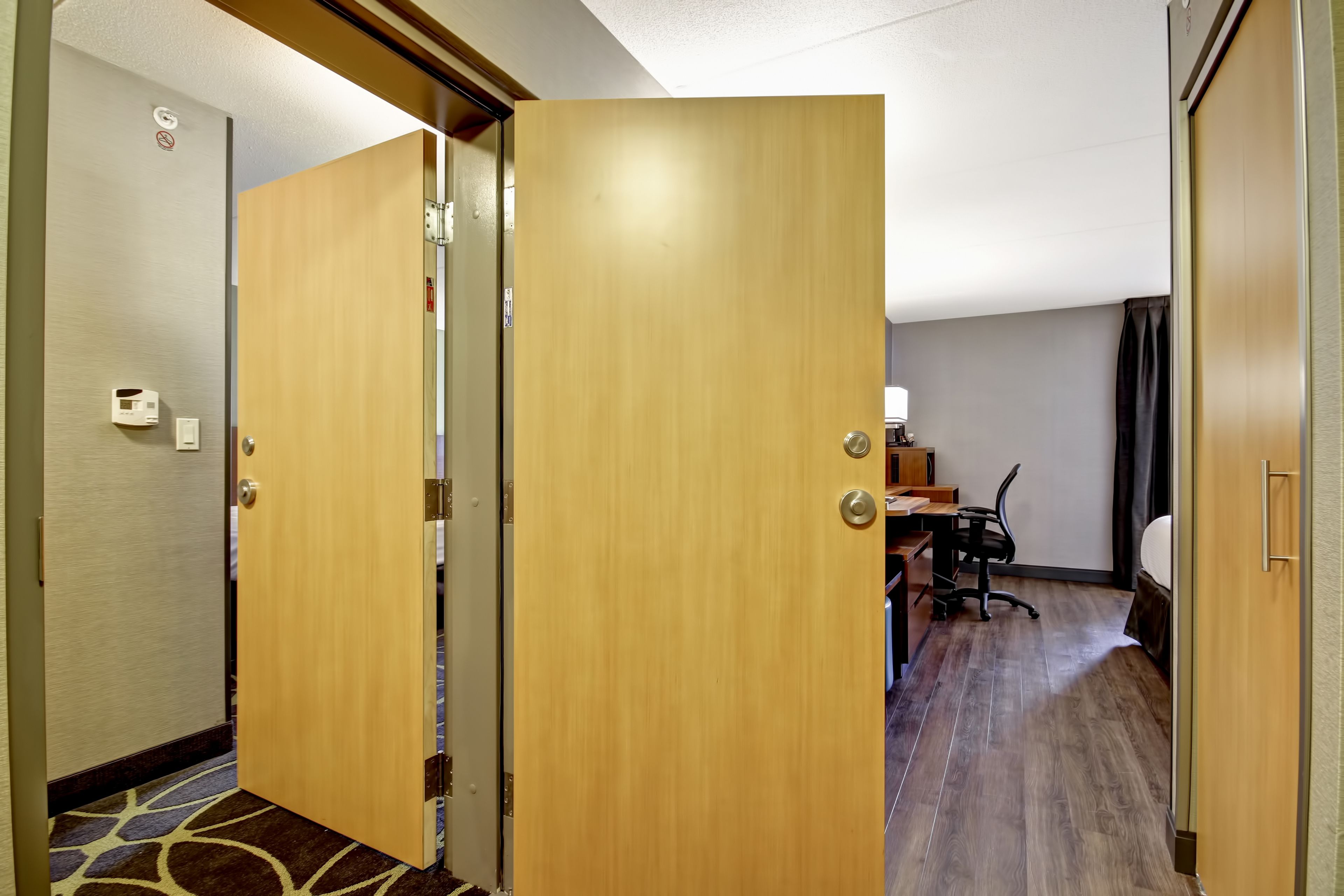 Una habitación de hotel con puerta de madera, un escritorio con silla y una cama.