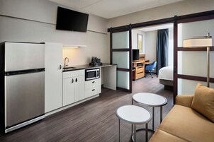 Habitación de hotel con kitchenette, cama, escritorio y televisor.