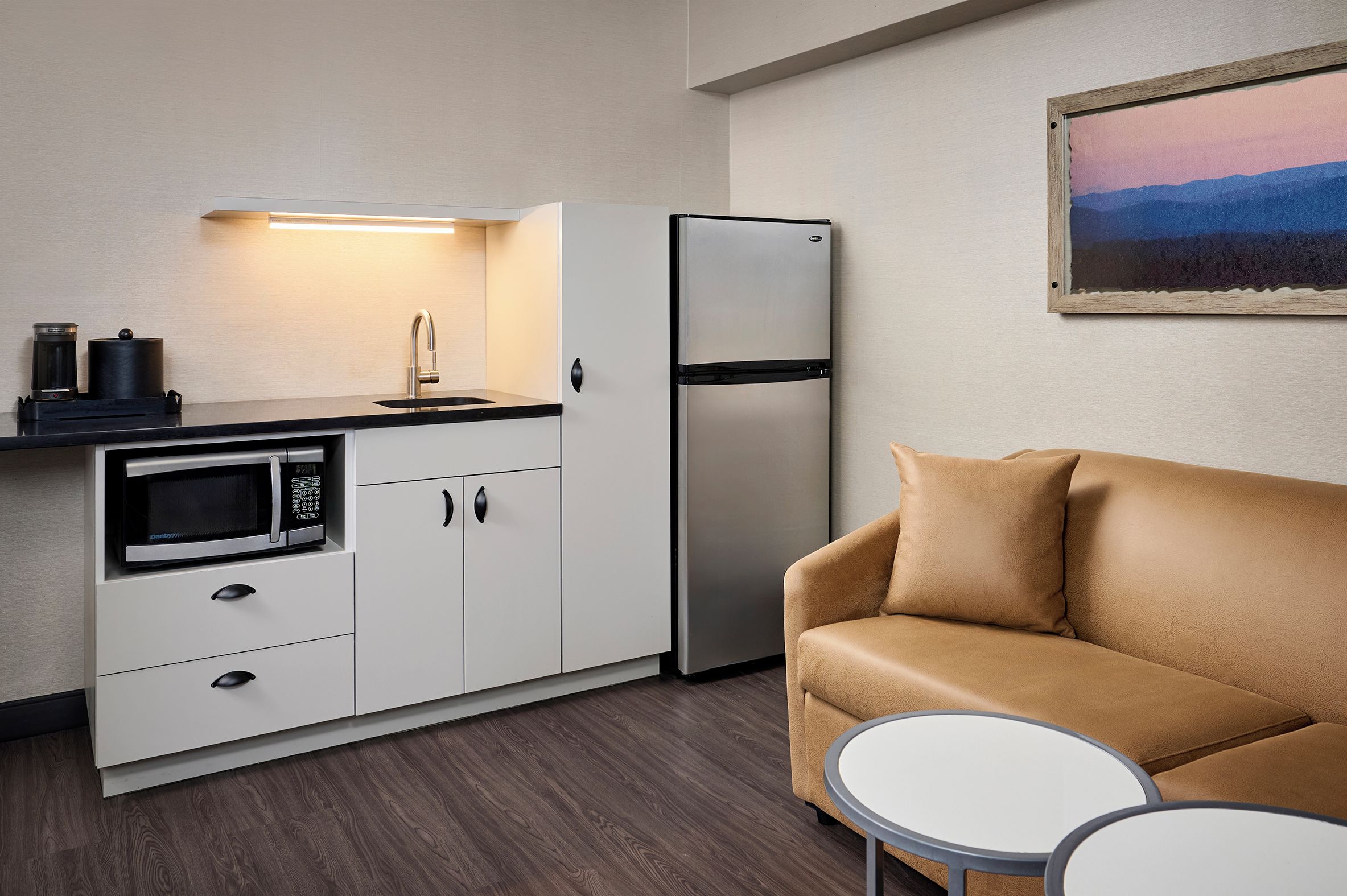 Eine kompakte Küchenzeile mit Mikrowelle, Kaffeemaschine und Kühlschrank. Im Wohnbereich befindet sich eine Couch und ein kleiner runder Tisch.