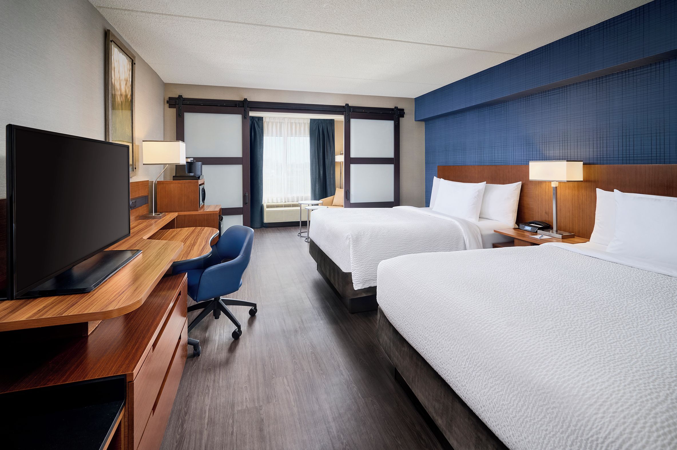 A hotel room with two beds, a desk with a TV, a chair, and a window with curtains.